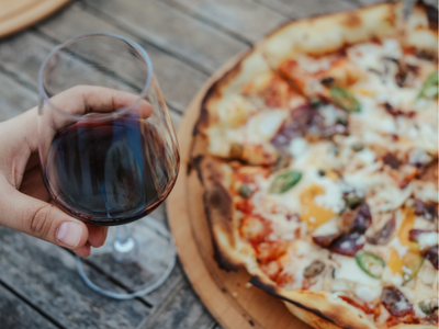 Glass of red wine being held by pizza