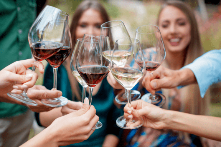 A group of people clinking wine glasses together in a celebratory toast outdoors.