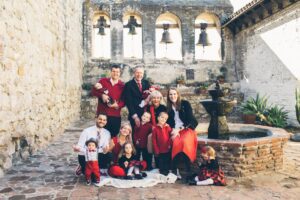 A family in red and black outfits poses by a stone fountain in a historic courtyard with bell arches.