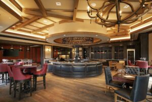 Elegant restaurant interior with round central bar, wine rack, wooden beams, and red and black upholstered chairs.