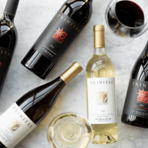 Bottles and glasses of Trinitas red and white wine displayed on a marble surface.