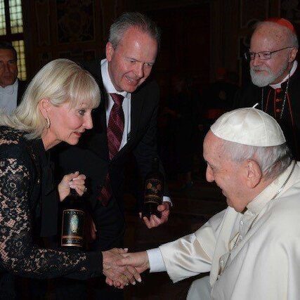A woman shakes hands with Pope Francis as others look on in a formal, indoor setting.