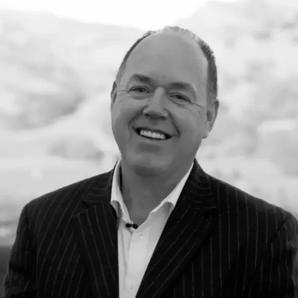 Smiling man in a pinstripe suit jacket, standing outdoors with a blurred background.